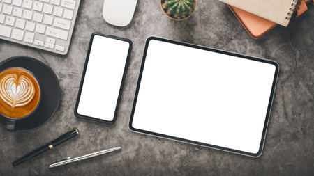 Dark office desk workplace with blank screen tablet and smartphone, keyboard, mouse, notebook, pen and cup of coffee, Top view flat lay with copy space.の写真素材