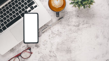 White desk workplace with blank screen smartphone, pen, eyeglass, laptop and cup of coffee, Top view...