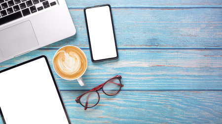 Office desk workplace with blank screen tablet and smartphone, laptop computer, eyeglass and cup of...