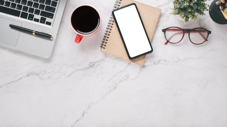 White office desk workplace with blank screen smart phone, laptop, pen, eyeglass, notebook and cup...