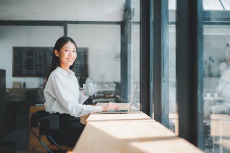 Portrait of young business woman working on laptop in office, Woman holding coffee cup in office.の写真素材