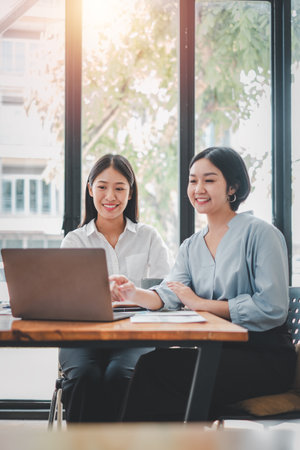 Two businesswoman working together on laptop computer. Creative female executives meeting in an office using laptop pc and smiling.の写真素材