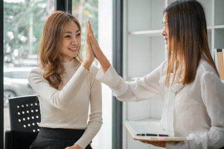 Businesswoman giving a high five to female colleague in meeting. Business professionals high five during a meeting in boardroom.の写真素材