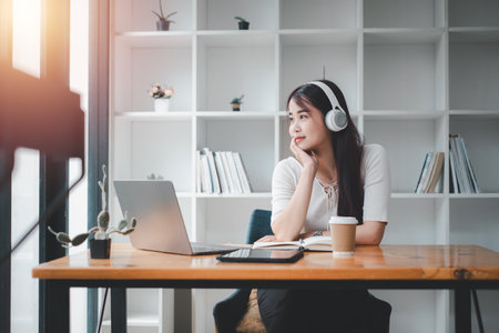 Pretty young woman listening to music with laptop computer and relaxing while sitting on chair at home.の写真素材