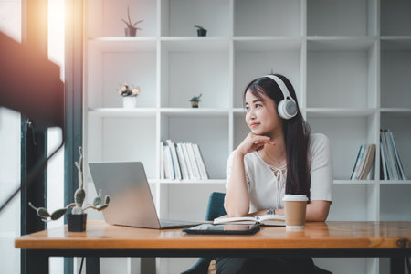 Pretty young woman listening to music with laptop computer and relaxing while sitting on chair at home.の写真素材