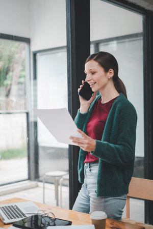 Happy businesswoman talking on mobile phone while analyzing weekly schedule in her notebook.の写真素材