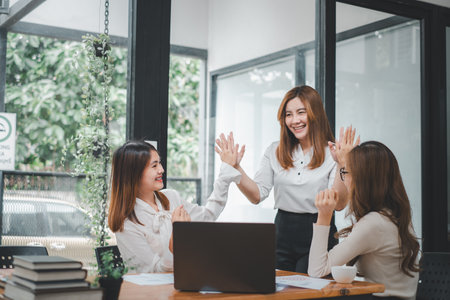 Business team giving a high five to female colleague in meeting. Business professionals high five during a meeting in boardroom.の写真素材