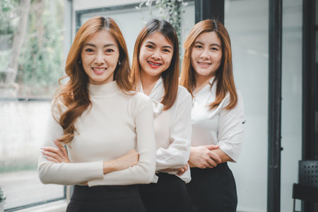 Three happy beautiful business woman diverse sitting on office desk and looking at camera, portraitの写真素材