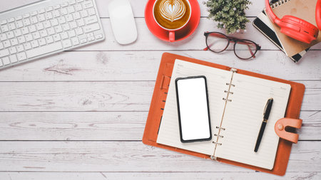 White wooden desk workplace with blank screen smartphone, notebook, pen, keyboard, mouse, eyeglass, headphone, notebook and cup of coffee, Top view flat lay with copy space.の写真素材