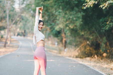 Fitness concept, Cheerful young woman in sportswear stretching arms while enjoying a workout in a peaceful park setting.の写真素材