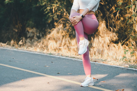 Fitness concept, Close-up view of a woman in pink leggings doing a quad stretch on a quiet road,...