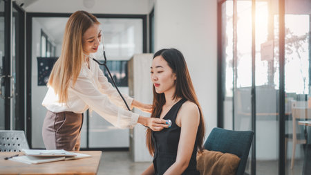 A healthcare professional conducts a routine stethoscope checkup on an employee in a sunny, contemporary office environment.の写真素材