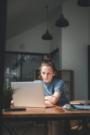 A woman, deeply engrossed in her work, leans forward towards her laptop screen, her expression one of intense focus and determination in a well-lit modern office.の写真素材
