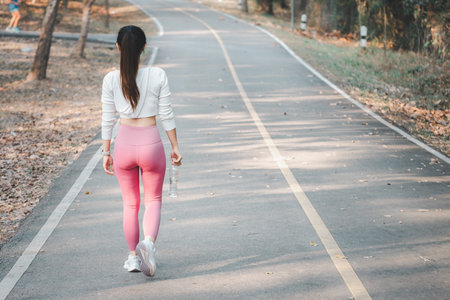 Back view of Beautiful fitness athlete woman holding water bottle after work out exercising on sunrise morning in public park.の写真素材