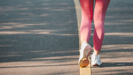 Close-up of a runner's legs in vibrant pink leggings, emphasizing motion and fitness on a sunlit...