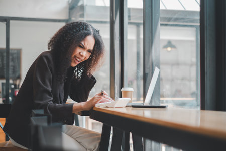 A cheerful businesswoman enjoys a light-hearted moment while working on her laptop at a cafe, her laughter adding a touch of joy to the professional setting.の写真素材
