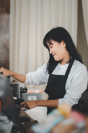 A smiling barista in a black apron arranges cups at a coffee shop, her pleasant demeanor adding...