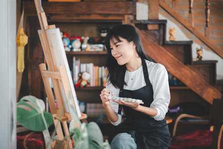 An aspiring artist with a serene expression delicately applies brush strokes to a canvas in a cozy, well-decorated studio filled with creative inspiration.の写真素材