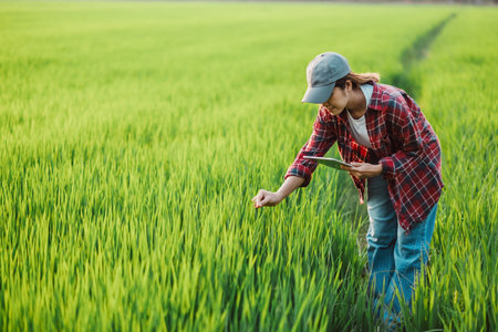 Female agronomist with a digital tablet is inspecting the growth of crops in a lush green field...