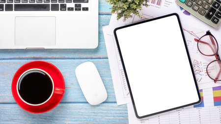 A laptop, a mouse, a red coffee cup, and a tablet are on a wooden desk. Concept of productivity and...