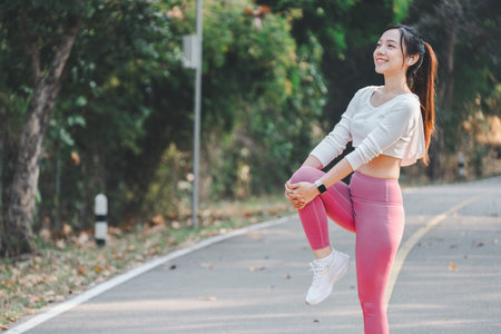 Cheerful young woman performs a leg stretch on a peaceful road, enjoying her morning fitness routine...
