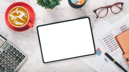 A professional workspace scene featuring a blank tablet screen, a cup of latte art coffee in a red...