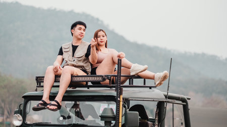 Young couple sits atop a safari vehicle, casually dressed, enjoying the view of a hazy, mountainous landscape.の写真素材