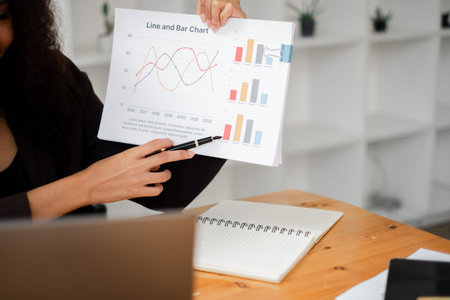 Close-up of a businesswoman's hands pointing at a line and bar chart, explaining business trends and...