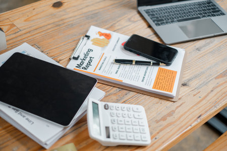 Well-organized work desk displaying a marketing report, tablet, smartphone, calculator, and laptop, ready for business analysis.の写真素材