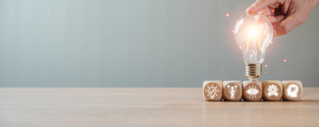 Creativity concept, Hand holding lightbulb and wooden block  on desk with innovation, motivation, vision, reward and problem solving icon on virtual screen.の写真素材
