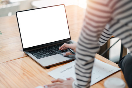 A woman is typing on a laptop with a blank screen. She is sitting at a desk with a piece of paper in front of herの写真素材