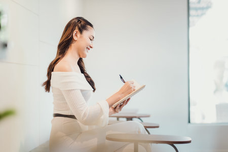 A woman is sitting in a chair and writing in a notebook. She is smiling and she is enjoying herself....