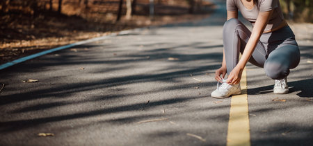 A woman is kneeling on the road, putting on her shoes. Concept of determination and focus as the woman prepares for her runの写真素材