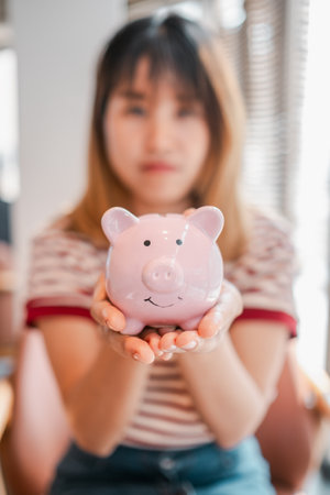 A woman is holding a pink piggy bank. She is wearing a striped shirt. The piggy bank is pink and has a smiley face on itの写真素材