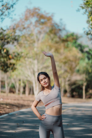 A woman is doing a yoga pose on a road. She is wearing a grey top and grey pantsの写真素材