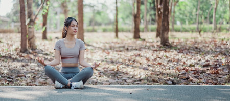 A woman is sitting on the ground in a park, meditating. The scene is peaceful and serene, with the woman's focus on her breathing and the natural surroundingsの写真素材