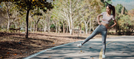 Young woman in athletic wear exercising outdoors, performing a side leg lift on a park path...