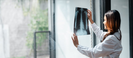 A female doctor in a white coat examines a chest X-ray in a bright, modern medical facility with...
