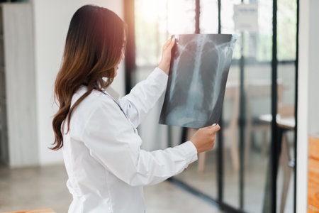 A female doctor in a white coat examines a chest X-ray in a bright, modern medical office.の写真素材