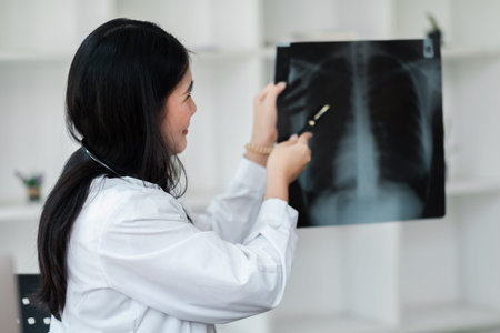 A woman doctor is looking at a chest x-ray. She is holding a pair of scissors and pointing to a spot...