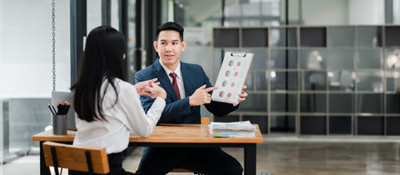Two professionals in a modern office setting discussing a business presentation with charts and graphs.の写真素材