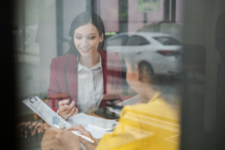 Two professional women engaged in a business meeting, discussing documents in a modern office environment.の写真素材