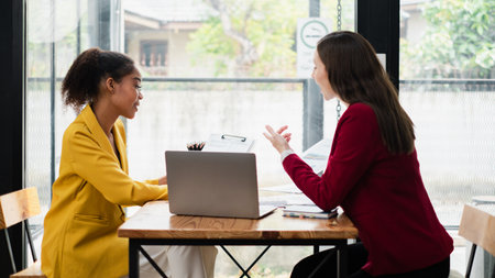 Two professional women having a business meeting in a contemporary cafe, discussing documents and working on a laptop.の写真素材