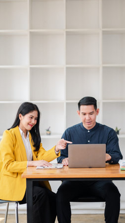 Two professionals collaborating on a project using a laptop in a modern office setting with white...