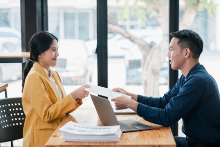 Two professionals engaged in a business meeting, exchanging documents in a modern office with natural light.の写真素材