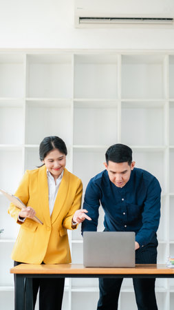 Two professionals working together in a bright, modern office, focusing on a laptop and discussing documents.の写真素材