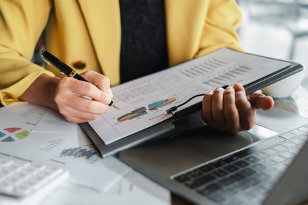 Close-up of a business professional analyzing financial data and charts with a pen in an office...