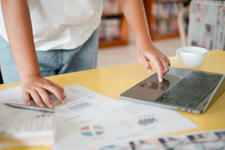 Close-up of a person working on a laptop and analyzing financial charts and graphs on a desk.の写真素材
