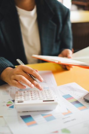 Close-up of a business professional using a calculator and reviewing financial documents at a desk.の写真素材