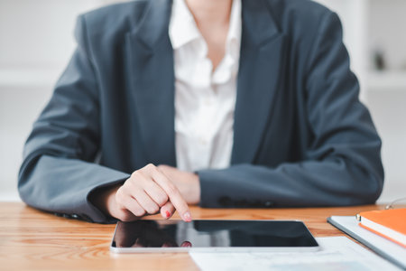 Close-up of a business professional in a suit using a tablet at a wooden desk, emphasizing technology in a modern office setting.の写真素材